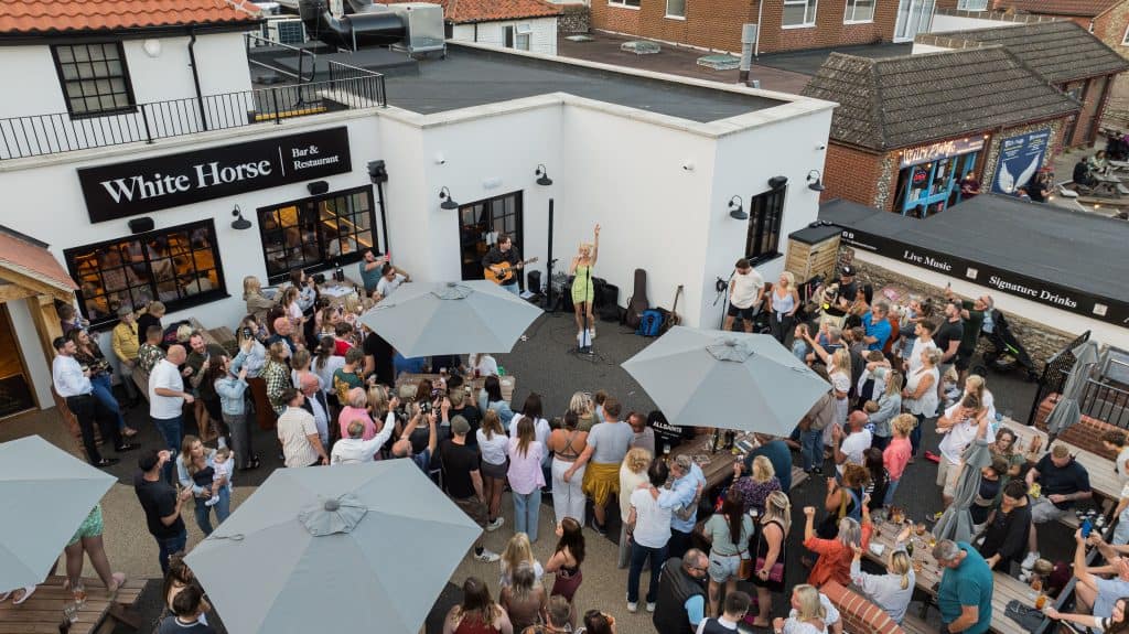 Aerial view of White Horse Bar's outdoor terrace with guests gathered under parasols during a busy event