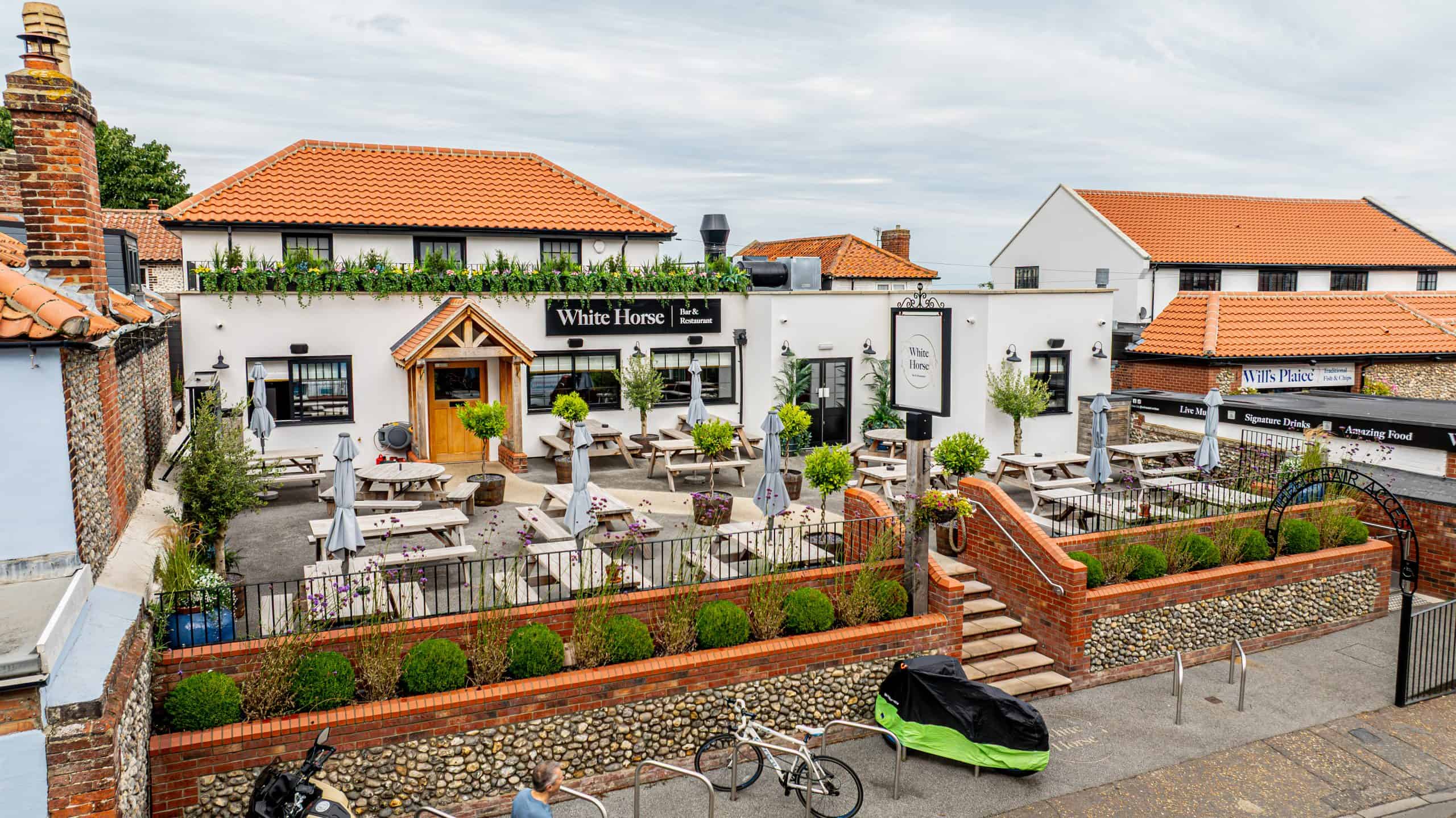 White Horse Bar exterior with terrace seating, planters and green spaces, East Runton