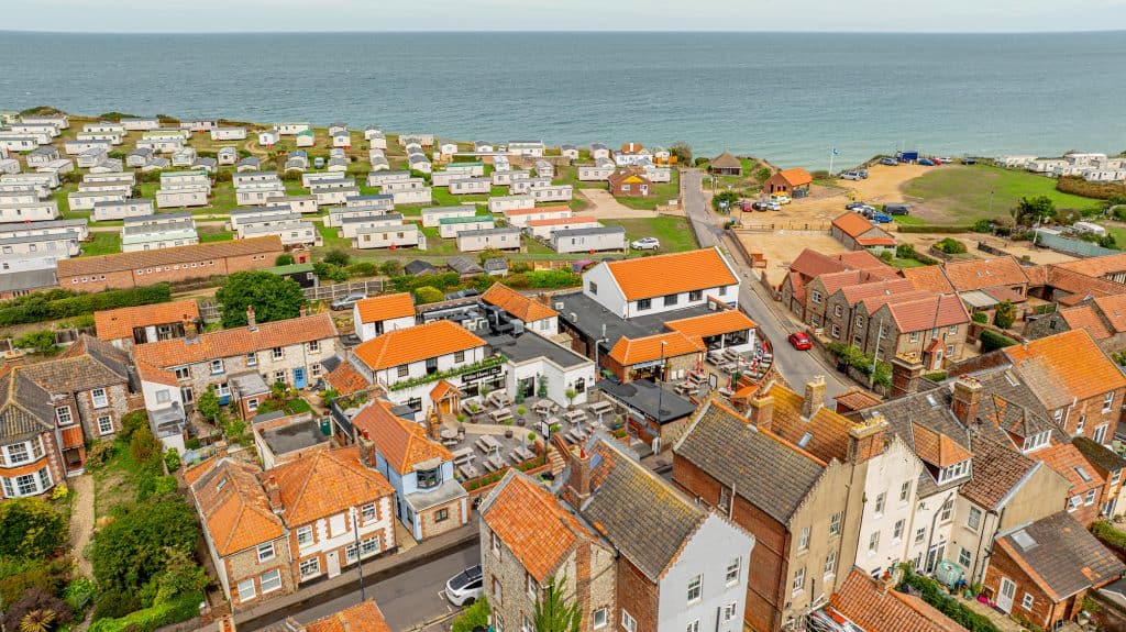 Aerial view of East Runton village with traditional houses, orange roofs, and caravans stretching toward the North Sea coastline.