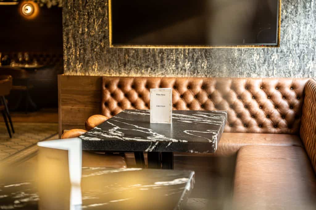 Tan leather banquette seating beside black marble table in bar dining room with warm lighting and textured wall panelling.