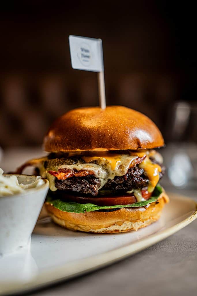 Gourmet burger with caramelised onions, melted cheese and lettuce on brioche bun, served on white plate with flag marker.